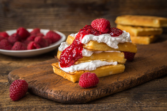 Belgian waffles with raspberries and double cream on rustic table.
