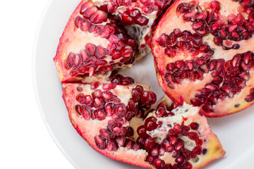 Broken red ripe pomegranates in white plate on white background