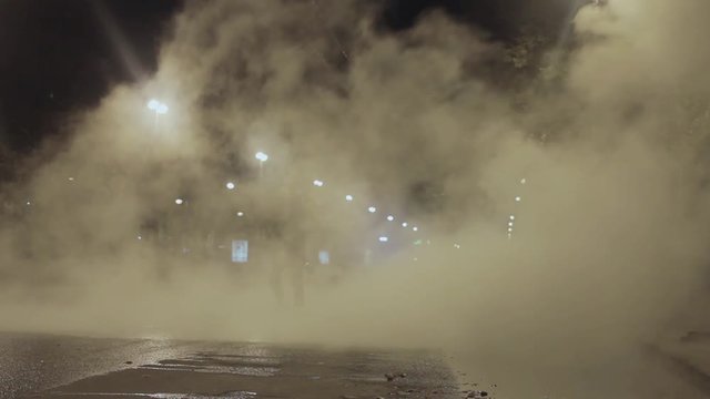 Man walk toward camera in night city street covered in steam from drain accident
