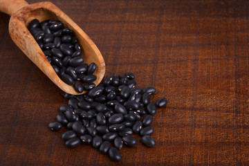Black beans in scoop on wooden background