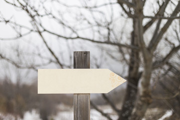 Blank wooden sign under snow with snow covered woods background.