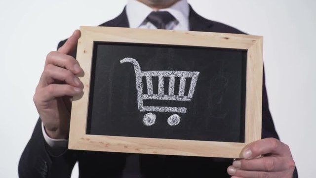 Shopping cart on blackboard in businessman hands, retail trade, consumer bundle