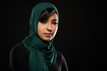 Naklejka premium Portrait of a beautiful Muslim woman dressed in hijab on a black background in photo studio.