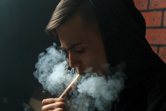 Young handsome white guy is admiting puffs of steam from the electronic cigarette. Vaping. Teenager listening to music.