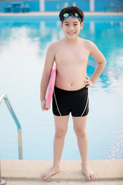Happy asian boy in swimsuit coming up the pool