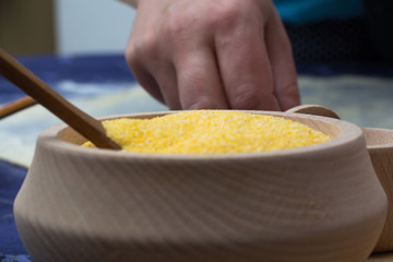 Corn flour in the wooden bowl with spoon on the home table.