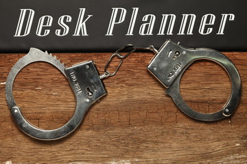 The chrome metal handcuffed put on the hardwood brown color represent the crime and punishment...