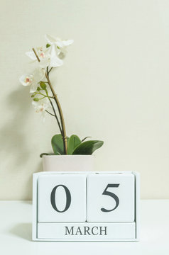 Closeup white wooden calendar with black 5 march word with white orchid flower on white wood desk and cream color wallpaper in room textured background , selective focus at the calendar