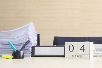 Closeup white wooden calendar with black 4 march word on blurred brown wood desk and wood wall textured background in office room view with copy space , selective focus at the calendar