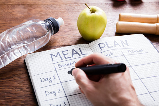 Person Hand Filling Meal Plan In Notebook