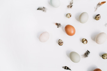 White and brown Easter eggs, quail eggs and feathers on white background. Flat lay, top view. Traditional spring concept.