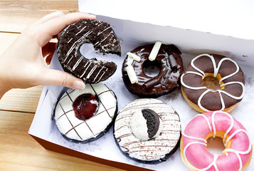colorful donuts in a box with chocolate chip, pink glazed on wood background.