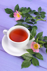 Cup of tea and wild rose flower on purple boards