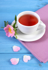 Fototapeta na wymiar Cup of tea and wild rose flower on blue boards