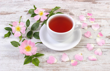 Cup of tea and wild rose flower on old rustic wooden background