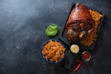 Whole baked pork knuckle and braised cabbage on a scratched metal surface, high angle view with copyspace - obrazy, fototapety, plakaty