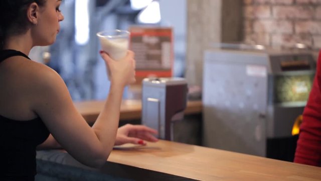 Barman In Fitness Center Give Protein Shake To Young Slim Beautiful Woman. In Sports Center Redheaded Lady With Ponytail In Black Sportswear Sitting At Wooden Bar, Drink Nutrition Milk Cocktail As