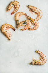 Raw uncooked tiger prawns on chipped ice over light grey background, top view, copy space, vertical composition. Fresh seafood concept