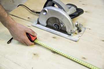 Building tape measure against background of plywood circular saw