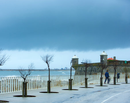 Storm weather. A man with an umbrella goes a sidewalk in the rain. Ocean waterfront embankment  park. Porto. Portugal.