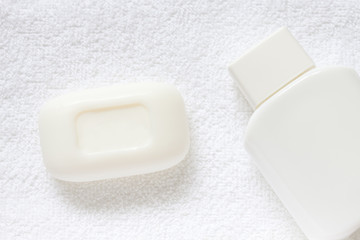 Cosmetic bottle with body lotion and bar of cream-soap on fluffy bath towel. Spa and beauty motif wallpaper mock up