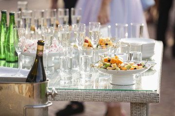 Party outdoors. People stand near the table with glasses of champagne and fruits.