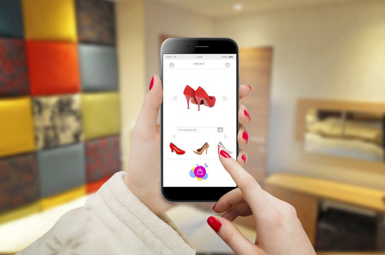 Modern black smartphone in female hands with online shopping concept interface, with blurred apartment in background