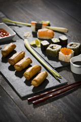 Frühlingsrollen und Sushi auf schwarzen Holztisch