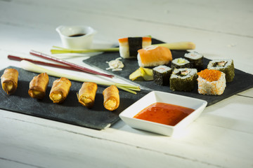 Frühlingsrollen und Sushi auf schwarzer Schieferplatte angerichtet