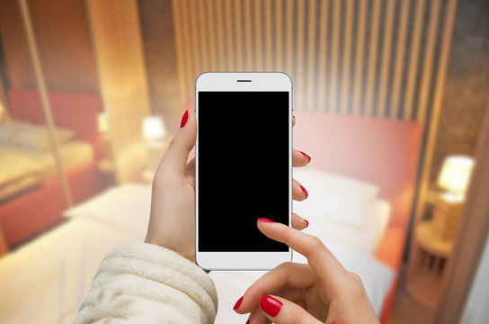 Women in hotel room holding phone with blank screen in hand 