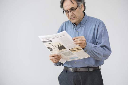 Senior man reading newspaper on gray background