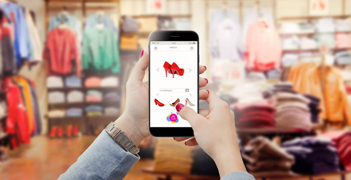 Women in clothing store holding phone in hands and searching online shoes 
