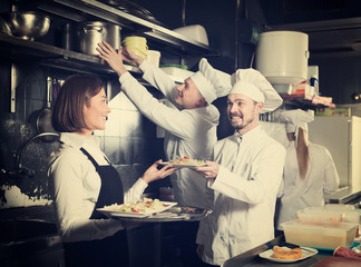 attractive woman waiter collecting dishes from restaurant’s kitchen