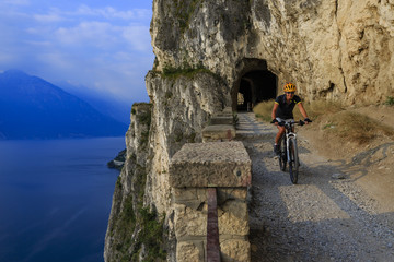 Mountain biking woman at sunrise over Lake Garda on path Sentiero della Ponale, Riva del Garda, Italy