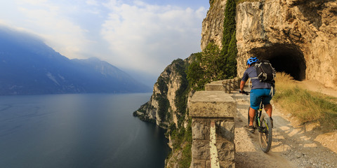 Mountain biking man at sunrise over Lake Garda on path Sentiero della Ponale, Riva del Garda, Italy