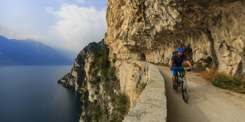 Mountain biking man at sunrise over Lake Garda on path Sentiero della Ponale, Riva del Garda, Italy