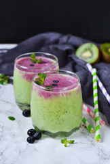 Homemade smoothies with kiwi, spinach and blueberries on a marble background with gauze