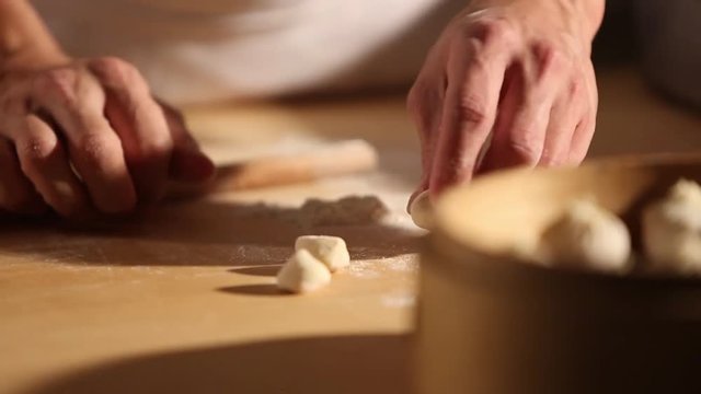A cook is making dumplings with his hands and is placing them in a bowl. He uses a bamboo steamer basket to place it on a pot of boiling water