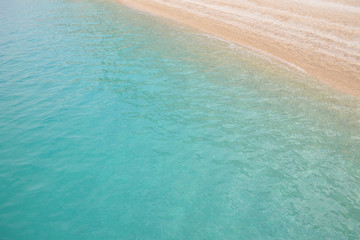 Seen from above emerald calm sea water reaching the sandy beach 
