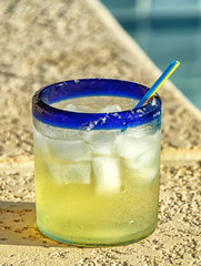 Margarita cocktail glass with ice cubes next to swimming pool; dedicated focus