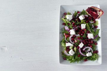 Fototapeta na wymiar Fresh healthy green salad with pomegranate seeds, onion and feta cheese. Top view, copy space