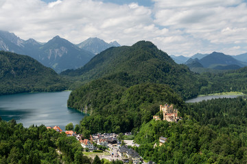Fototapeta na wymiar View from top to world-famous Hohenschwangau Castle (Schloss) and Alpsee lake from the cliff, Alps and clouds on background, Fussen, Bavaria , Germany
