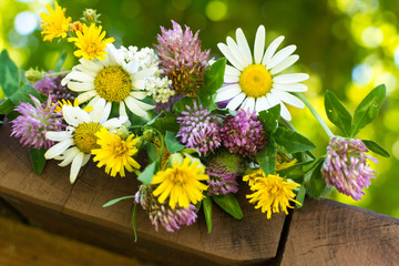 A closeup bouquet of wildflowers: clover, chamomile dandelion on wooden table, bokeh background