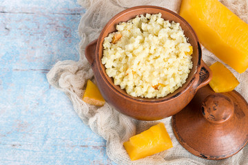 Millet porridge.   Dishes for Lent. Clay pot with millet gruel and pieces of fresh ripe pumpkins on an old napkin on a light wooden table.
