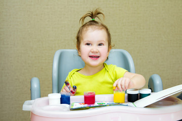 Baby girl sitting on a chair and opens the finger paints