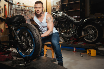 Obraz na płótnie Canvas Handsome motorcyclist posing in the workshop