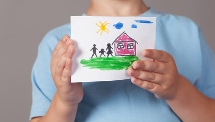 Child holds a drawn house with family in his hands