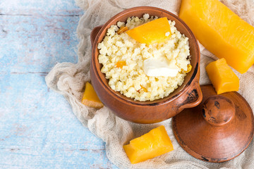 Millet porridge.    Clay pot with millet gruel and pieces of fresh ripe pumpkins on an old napkin on a light wooden table.