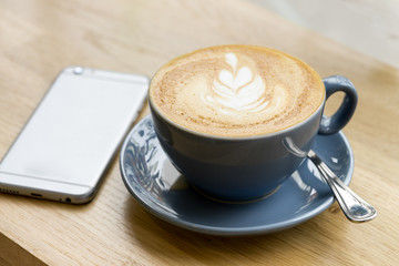 dark blue cup of coffee with art design made hot milk hand phone table
