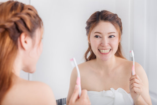 woman in bath towel brushing teeth with mirror in bathroom